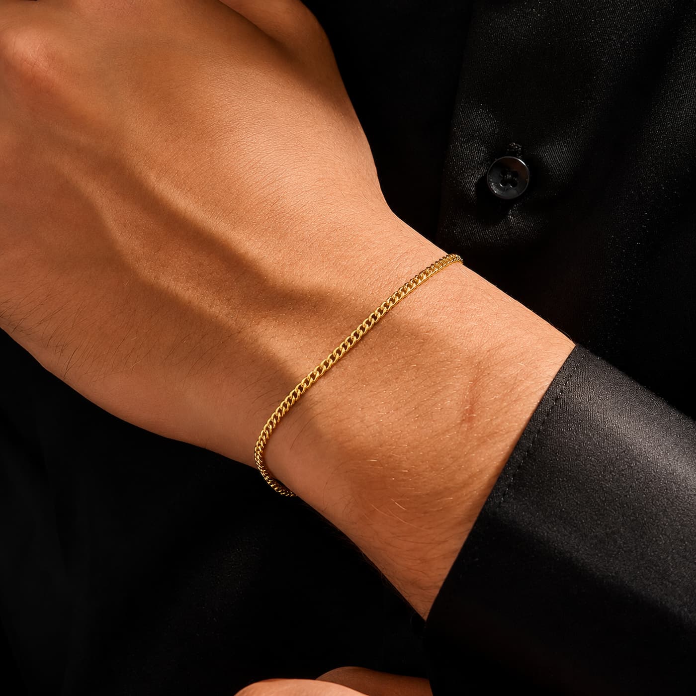 A close-up of a person's wrist wearing a delicate gold chain bracelet, set against a black shirt background.